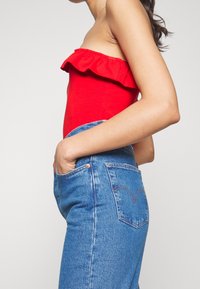 Bodysuit rojo sin tirantes con un escote con volantes, combinado con vaqueros de tiro alto azul con un diseño clásico de cinco bolsillos y detalles de costura.