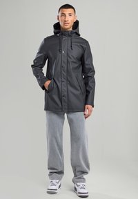 Black waterproof jacket with a hood, snap buttons, and side pockets; paired with light gray wide-leg pants and white athletic shoes.