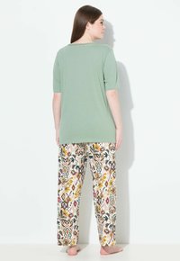 Lichtgroen T-shirt met korte mouwen en een gestructureerde halslijn, gecombineerd met loszittende broek in crèmekleur, bruin en een meerkleurig bloemenpatroon.