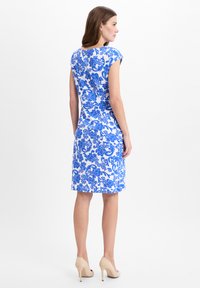 Blue floral-patterned dress on a model, featuring a fitted silhouette and cap sleeves, with a knee-length hem and smooth fabric.