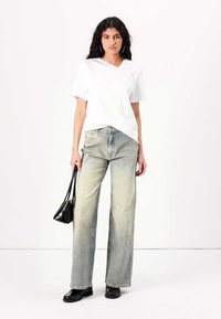 T-shirt bianco a maniche corte abbinato a jeans larghi in jeans chiaro. Il modello tiene una borsa nera. Scarpe basse, stile minimalista.