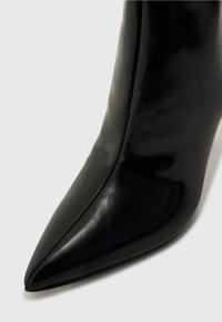 Botte de cheville en cuir noir avec un bout pointu et une texture lisse. Elle présente un design épuré et des détails de couture minimalistes le long des bords.