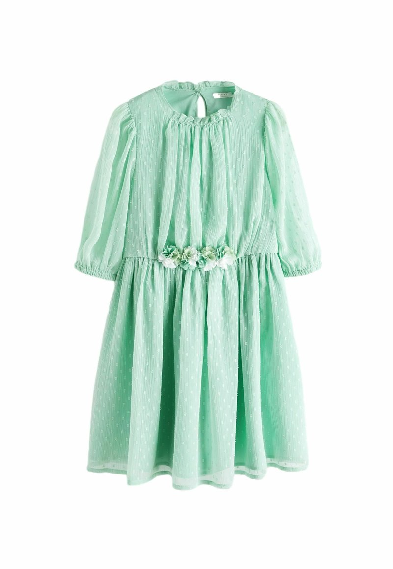 Robe vert menthe mi-longue avec manches bouffantes transparentes, tissu texturé, taille froncée et un bouquet de petites fleurs en tissu à la taille.
