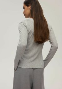 Szara bluzka z długim rękawem o prążkowanej teksturze. Posiada okrągły dekolt i dopasowany krój. Model nosi szare spodnie typu wide-leg.