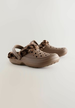 Brune træskor med en plysset, leopardmønstret kunstpelsrem, der har ventilationshuller og en bagrem for sikker pasform. Glat, tekstureret overflade.