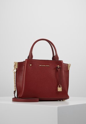 Mørkerød tekstureret lædertaske fra Michael Kors med dobbelte håndtag, guldkæde-rem og en lille hængelås-charm på en hvid piedestal.