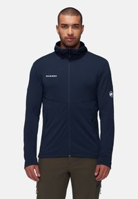 Marineblaues Reißverschlussjackett aus weichem Stoff, mit Kapuze, seitlichen Taschen und Logodetail auf der Brust und dem Ärmel.