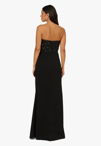 Czarna wieczorowa suknia bez ramiączek z dopasowanym koronkowym gorsetem i zwiewną spódnicą. Charakteryzuje się gładką fakturą i długą sylwetką.