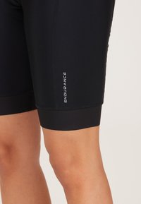 Schwarze Kompressionsshorts aus glattem Stoff mit figurbetontem Design und einem kontrastierenden "ENDURANCE"-Logo an der Seite.