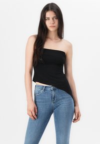 Svart strapless-topp med en figursydd design och en asymmetrisk fåll, kombinerad med ljusblå skinny jeans. Slät textur utan mönster.