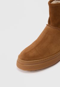 Ruskean mokkanahka ankle boot, jossa on sileä pinta, pyöreä kärki ja kumipohja. Korostaa erottuvaa ommelta sauman varrella ja lyhyttä varresta.