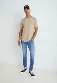 T-shirt en coton beige à manches courtes, assortie à un jean skinny bleu clair. Baskets noir et blanc avec semelles épaisses. Tenue simple et décontractée.