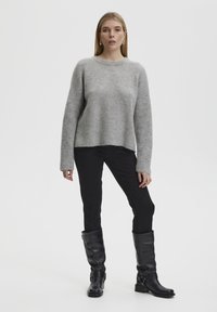 Suéter gris de punto con un corte relajado, mangas largas y escote redondo, combinado con pantalones negros ajustados y botas de cuero negro hasta la rodilla.