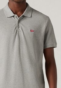 Grå polo t-shirt tillverkad av mjukt material, med en treknappsknäppning och en liten röd Levi's-logga på vänster bröst. Kort ärm.