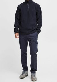 Sudadera de forro polar color navy con cuello de media cremallera y logo bordado; combinada con pantalones cargo navy que cuentan con bolsillos laterales y un corte relajado.