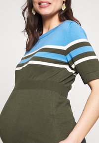 Maglione premaman con strisce blu, verdi e bianche. Dettaglio a costine in vita, maniche corte, silhouette aderente e tessuto morbido.