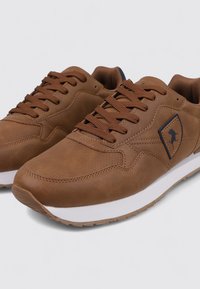 Zapatillas de cuero sintético marrón con una media suela blanca, punta redonda, diseño de cordones y un pequeño logotipo negro en el costado.