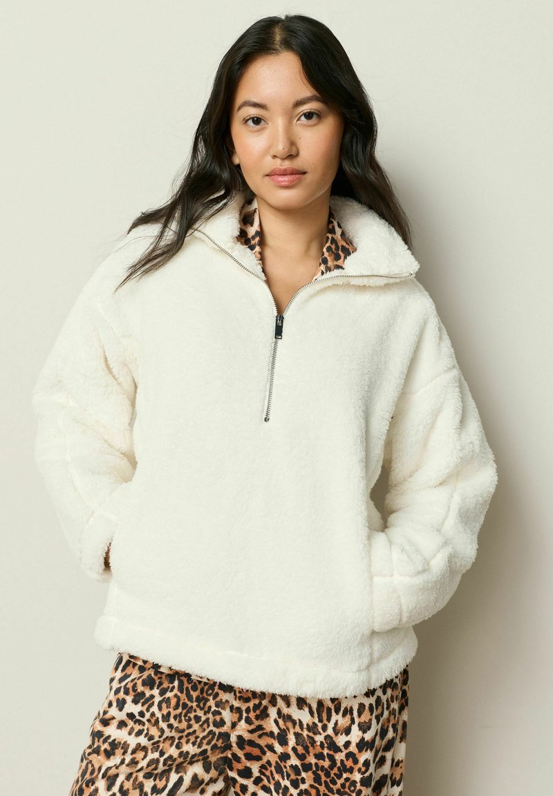 Hvid fleece-pullover med halvlukket krave og sænkede skuldre, parret med leopardmønstrede underdele. Blød tekstur og afslappet pasform.