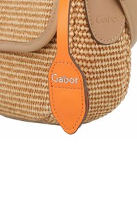 Sac à main en paille tissée avec des accents en cuir beige et une étiquette orange portant le logo Gabor. Surface texturée avec une forme arrondie.