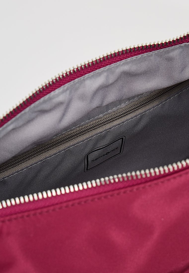 Bordeauxfarbene Stofftasche mit grauem Innenfutter, mit einem Reißverschlussverschluss und einer kleinen Tasche mit einem Etikett. Glatte Textur.