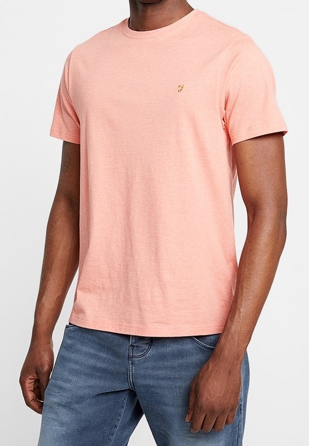 Homme portant un t-shirt uni rose clair à manches courtes et un jean bleu, debout les bras détendus le long du corps.