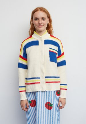 Krémový pletený kardigan s vícestrannými pruhy v červené, modré a žluté barvě. Má knoflíkovou přední část a čtvercovou kapsu v modré barvě.