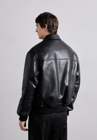 Veste bomber en cuir noir avec une texture lisse, des poignets et un ourlet côtelés, et un col classique. Présente des détails de couture subtils au dos.