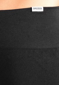 Leggings neri con una cintura a coste e una texture del tessuto liscia, con una piccola etichetta bianca con la scritta "SMILODOX" sulla parte superiore.