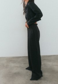 Svart kort jacka med knappar, matchad med högmidjade vida byxor med vertikala ränder. Slät tyg och skräddarsydd passform.