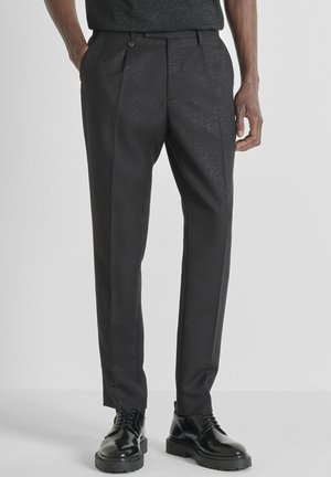 Zwarte broek met een gestructureerde afwerking, voorzien van een geplooide voorkant, platte zakken en een slank model. Gecombineerd met zwarte veterlaarzen.