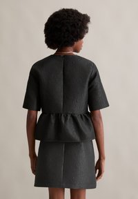 Melnas teksturētas auduma kleita ar īsām piedurknēm un pepluma jostu, ar aizmugures zipper slēgšanu un strukturētu siluetu.