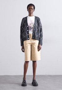 Melna kardigāna ar baltām pērlēm, balts grafiskais T-krekls, beigtas krāsas šorti un masīvi melni apavi veido slāņainu ikdienišķu tēlu.