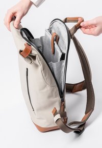 Beige Rucksack mit einem Reißverschluss, Innenfächern zur Organisation, braunen Lederelementen und Netz-Schulterriemen.