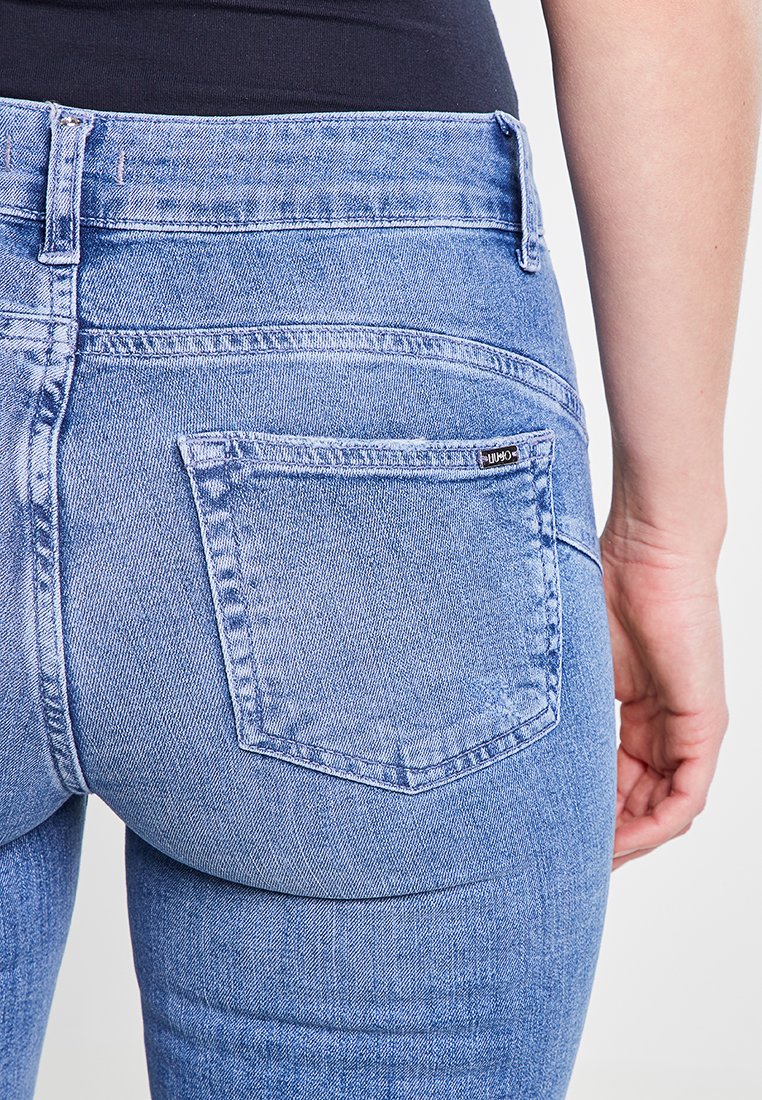 Jeans in denim blu magro con una texture leggermente sbiadita, caratterizzati da una tasca posteriore e dettagli di cucitura. La vita si posiziona sopra i fianchi.