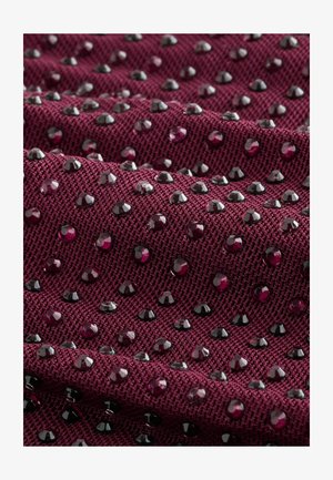 Burgundia tekstuuriga kangas, mis on kaunistatud läikivate mustade ja lillade detailidega, kus on mustriline paigutus tõstetud, paljandatud elementidega.