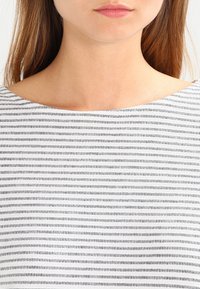 Grau- und weißgestreiftes Oberteil mit weitem Bootsausschnitt, leichtem Stoff und einer strukturierten Musterung aus kleinen horizontalen Linien.