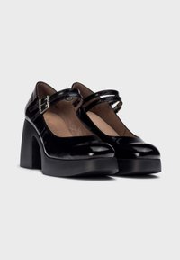 Zapatos Mary Jane de charol negro con dos correas con hebilla, tacones gruesos, punteras redondeadas y detalle de plataforma texturizada.