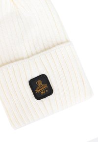 Beanie a maglia color crema con texture a coste e risvolto. Presenta una patch quadrata nera con un accento dorato nel logo.
