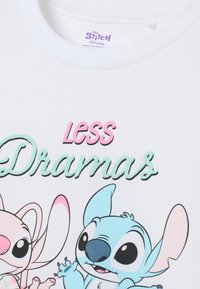 Witte katoenen t-shirt met gedrukt cartoonfiguren met zwarte contouren. De tekst luidt "Minder Drama" in roze en groen.
