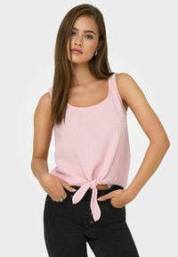 Lichtroze mouwloze top met een ronde halslijn en textuurstof, met een voorste strikdetail. Gecombineerd met donkere jeans.