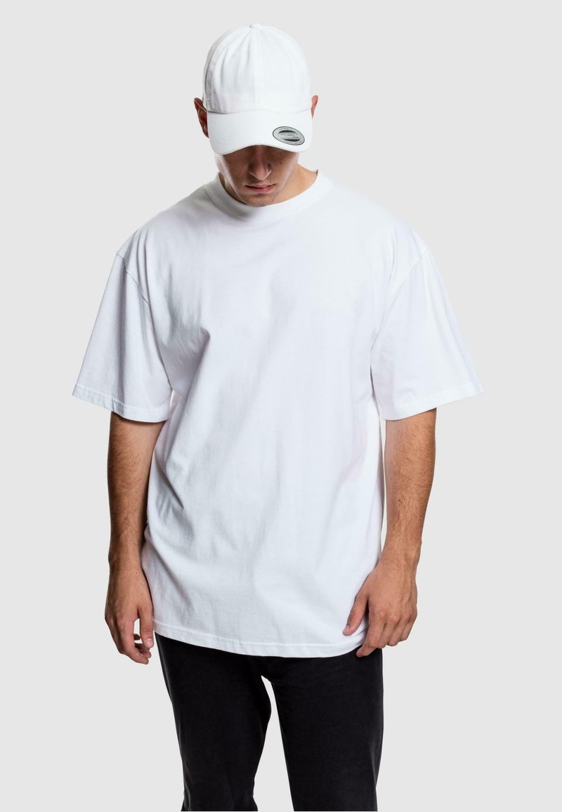 Weißes Baumwoll-T-Shirt mit kurzen Ärmeln, lockerer Passform, Rundhalsausschnitt, kombiniert mit einer passenden weißen Mütze und schwarzen Jogginghosen. Keine Muster.