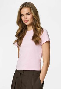 T-shirt en coton rose clair à manches courtes et col rond, associé à un pantalon taille haute marron foncé.