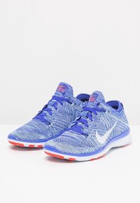 Zapatillas deportivas azules con parte superior de punto, patrón texturizado, símbolo de Nike en blanco y acentos rojos contrastantes en la suela y la lengüeta.