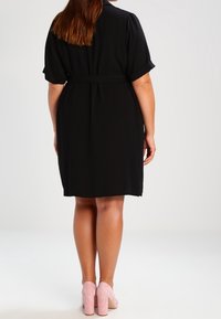 Czarna sukienka z paskiem, krótkimi, podwiniętymi rękawami, długości do kolan i gładką teksturą. Połączona z jasnoróżowymi, masywnymi obcasami.