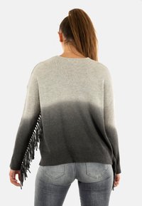Maglione grigio ombre con maniche a coste, dettagli in frange sull'orlo e una vestibilità rilassata. Il materiale sembra morbido e texturizzato.