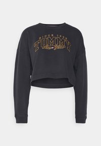 Svart kort sweatshirt med långa ärmar, med "TOMMY New York" broderat i guld och vitt över bröstet. Mjuk tygkänsla.