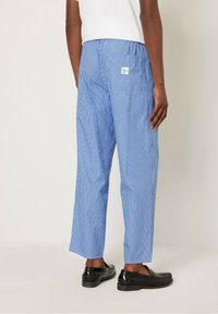 Pantalones de rayas azules y blancas con un corte relajado. Fabricados en tejido ligero, cuentan con un bolsillo trasero y una pequeña etiqueta verde.