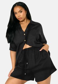 Ensemble deux pièces en lin noir comprenant une chemise à manches courtes avec boutons et un short à taille élastique avec poches. Design décontracté avec une coupe ample.