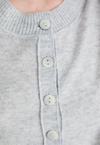 Lichtgrijze gebreide cardigan met vier ronde witte knopen dichtgemaakt, met een geribde kraag en een zachte stofstructuur.