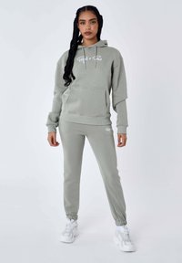 Lichtgrijze hoodie en joggers set van zacht materiaal. Bevat een voorkant zak, ribgebreide manchetten en een bedrukt logo op de borst en het been.